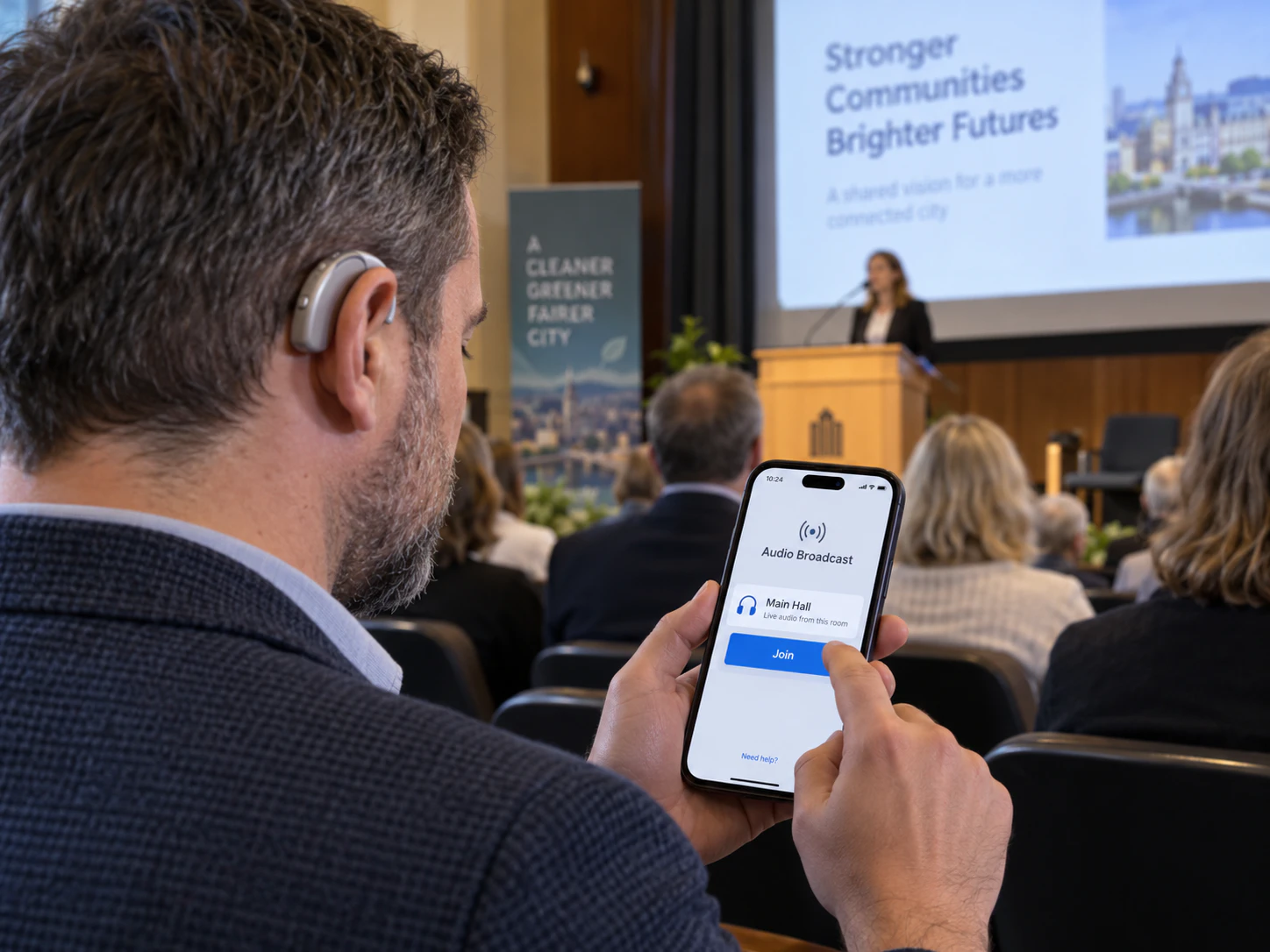 Audience member wearing a hearing aid joins the venue's audio broadcast on a phone during a presentation