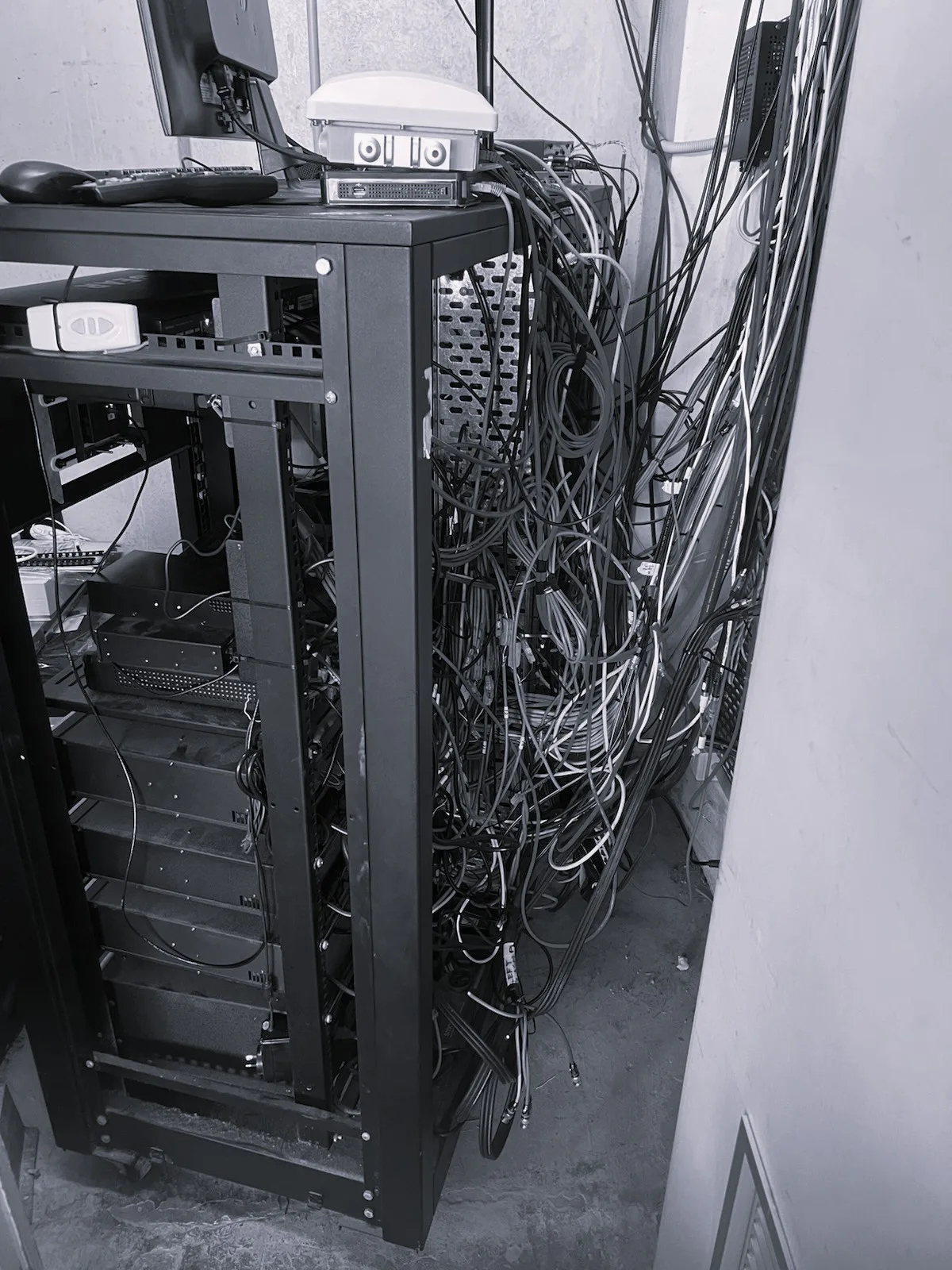 The existing equipment rack before the upgrade — unlabelled cabling running loose down the wall and across the floor