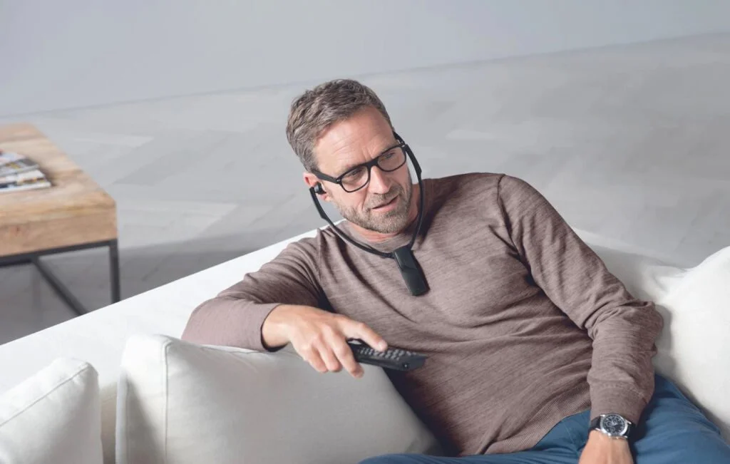 Man sitting on the lounge and wearing an assistive listening device to hear the TV