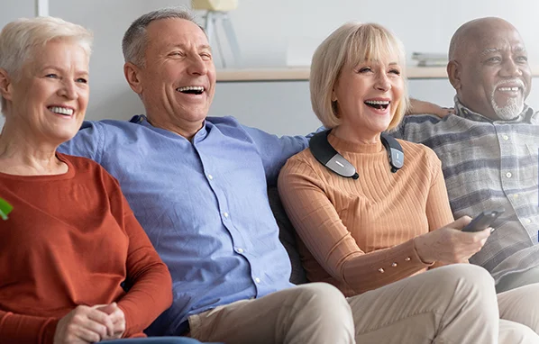 Group of elderly people watching TV and one woman is wearing the BeHear Proxy - Hearing Amplifier & Wireless Neck Speaker